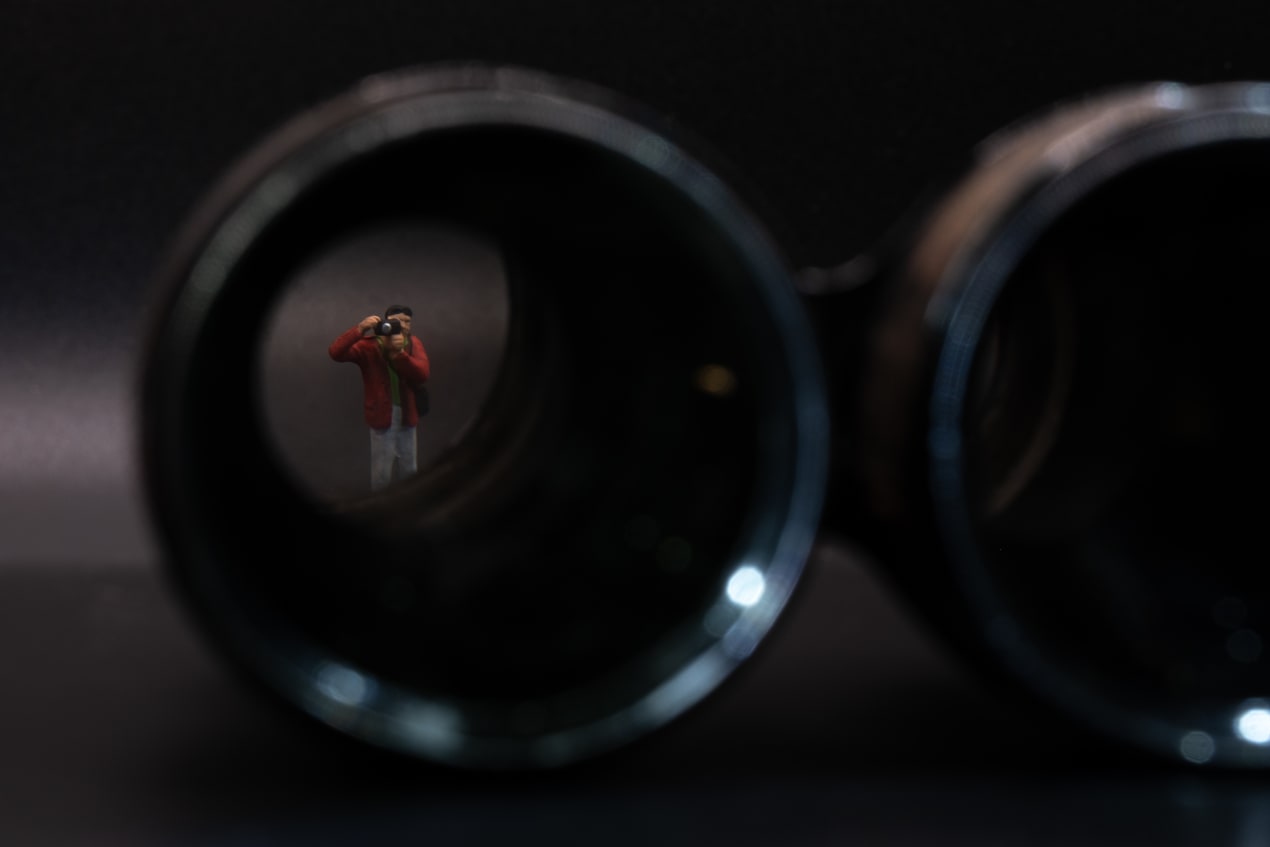 Photo of a miniature figure of a photographer, seen through the lenses of a pair of binoculars