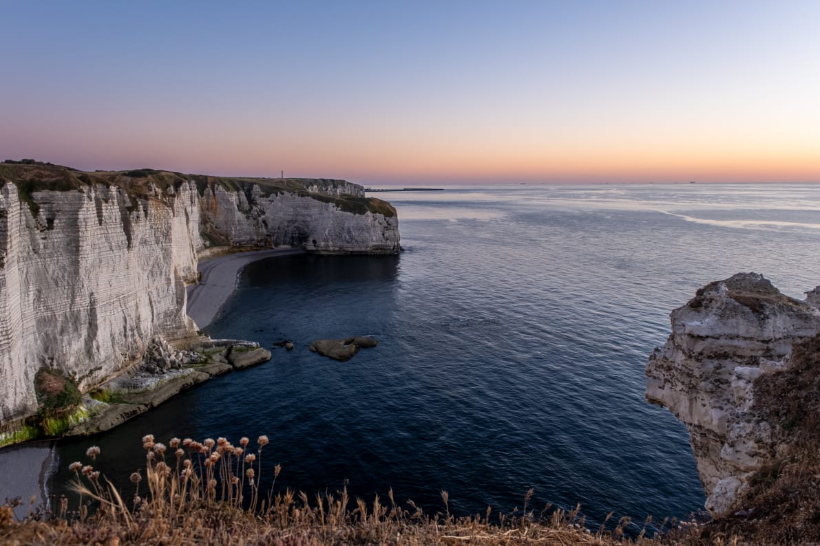 A scenic view of white chalk cliffs overlooking calm blue waters at sunset.