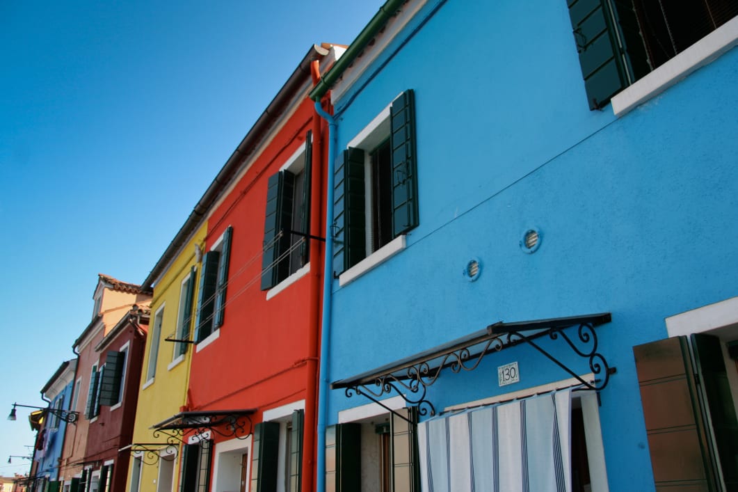 Colorful buildings with closed shutters under a clear blue sky.