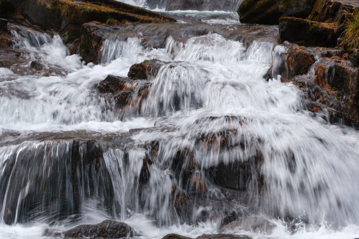 A cascade of water flowing over rocky steps, partially covered in moss.