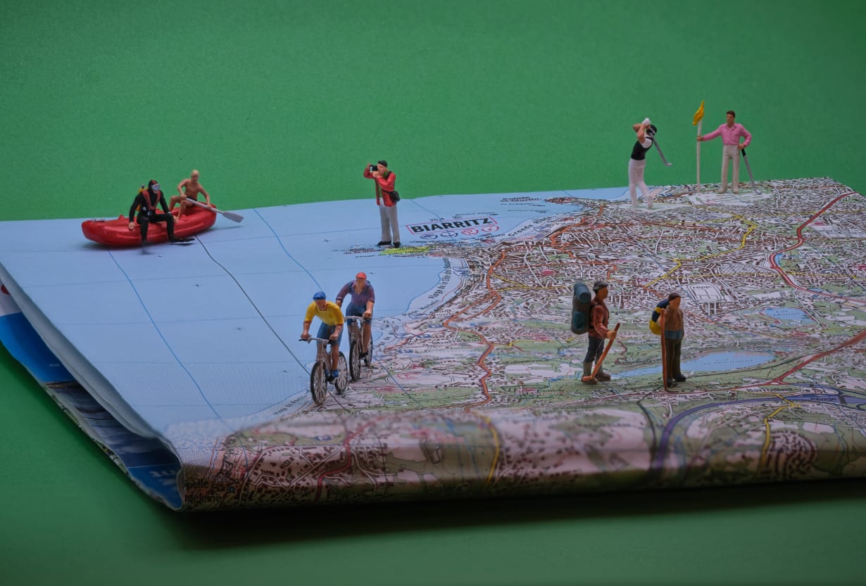 A close-up of a map featuring miniature figures engaged in various activities: two people in a canoe on the water, cyclists, a golfer, a photographer, and hikers.