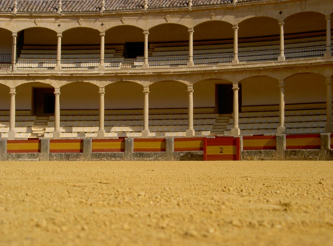 A bullring with empty seating and sand-covered arena in the foreground.