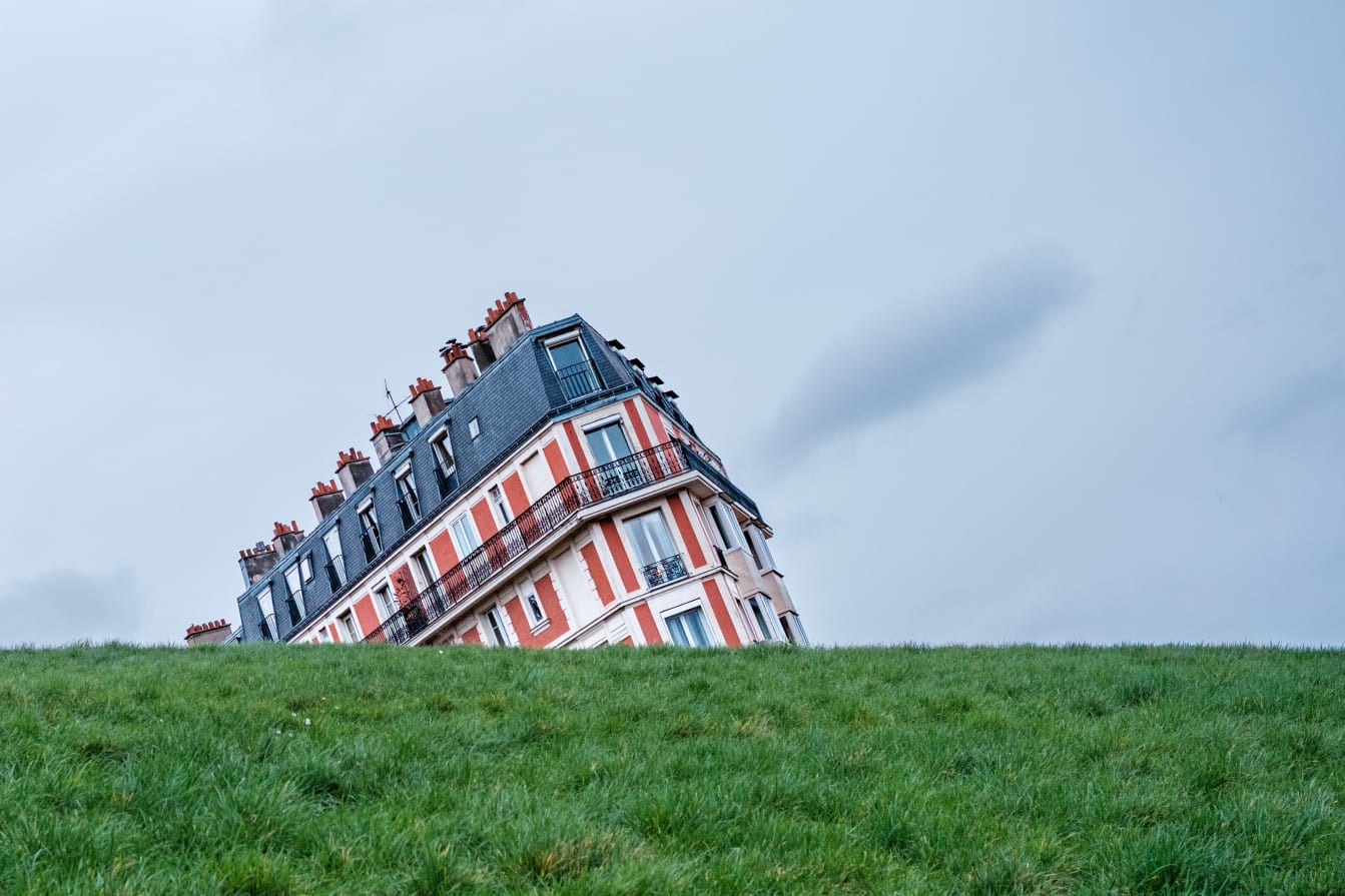 The upper part of an old building appears to be collapsing to one side and disappearing underground.