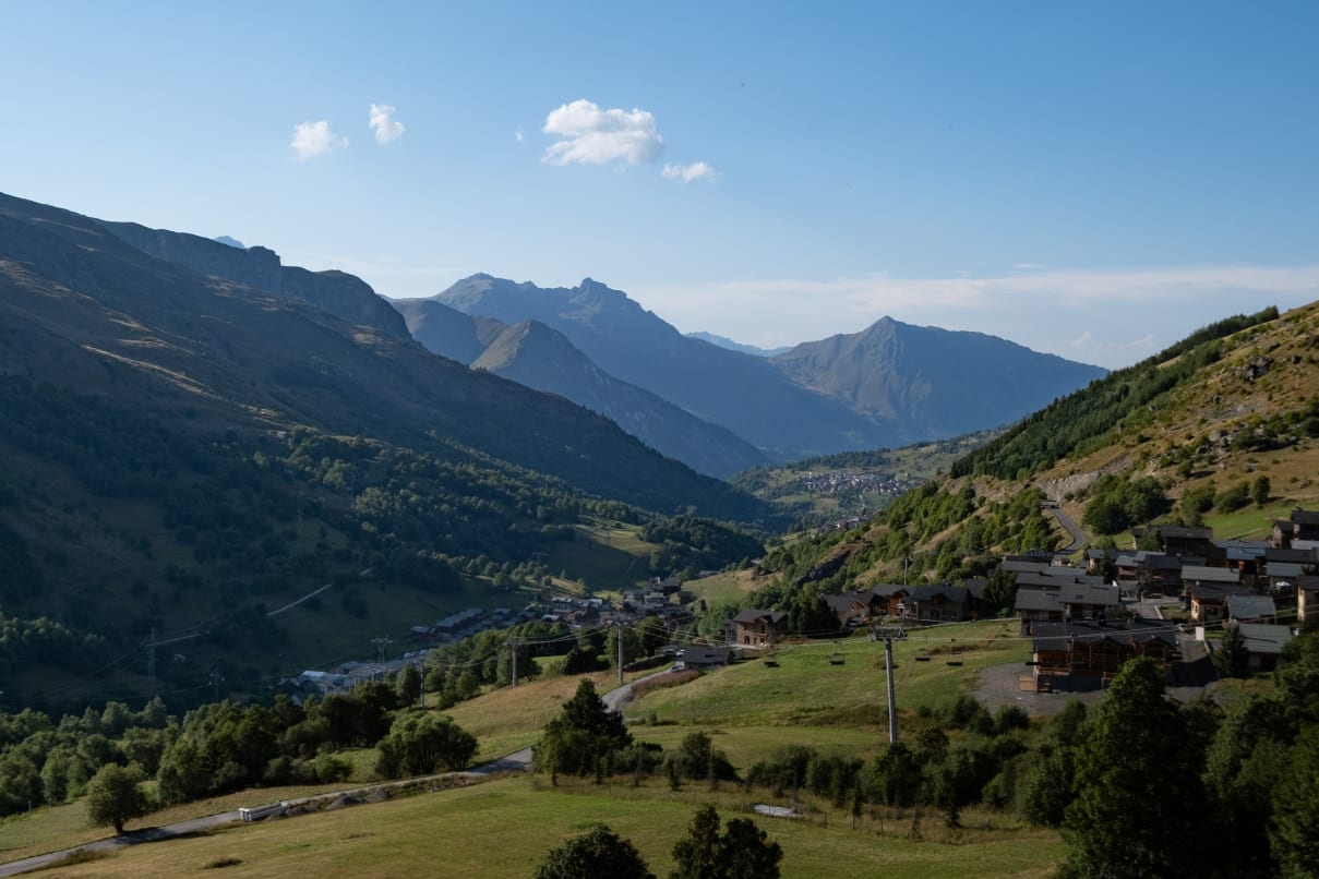 A picturesque mountain valley with lush greenery, scattered wooden houses, and a winding road.
