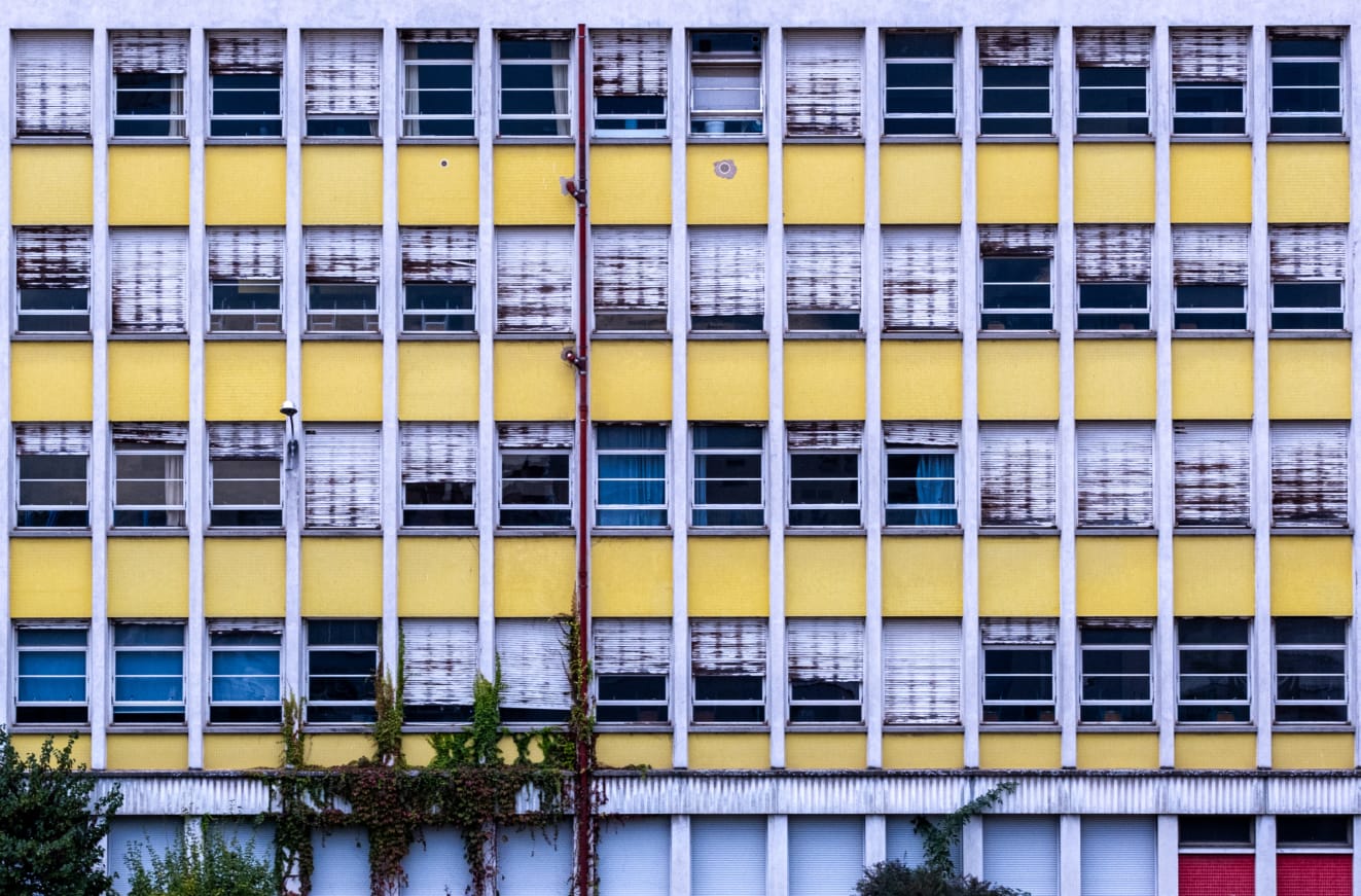 A facade of a building with yellow and white patterns and multiple windows, showing signs of weathering and disrepair.