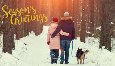 A couple and their dog walk down a snowy trail.