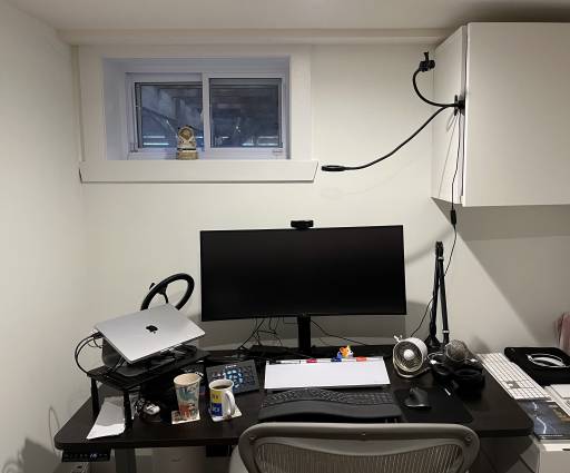 My desk setup. My Mac is on a stand on the left, a wide screen monitor in the middle, a microphone and boom on the right, and a keyboard, mouse, desk whiteboard, and Stream deck in the front. There are also ring lights around the desk for streaming.