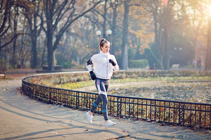 Woman going for a run in the park wearing gloves and listening to music