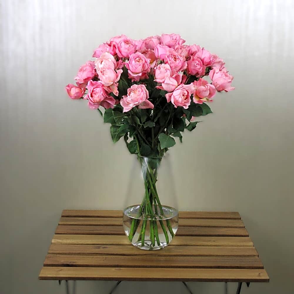 A vase of simple pink roses with white stones view 1