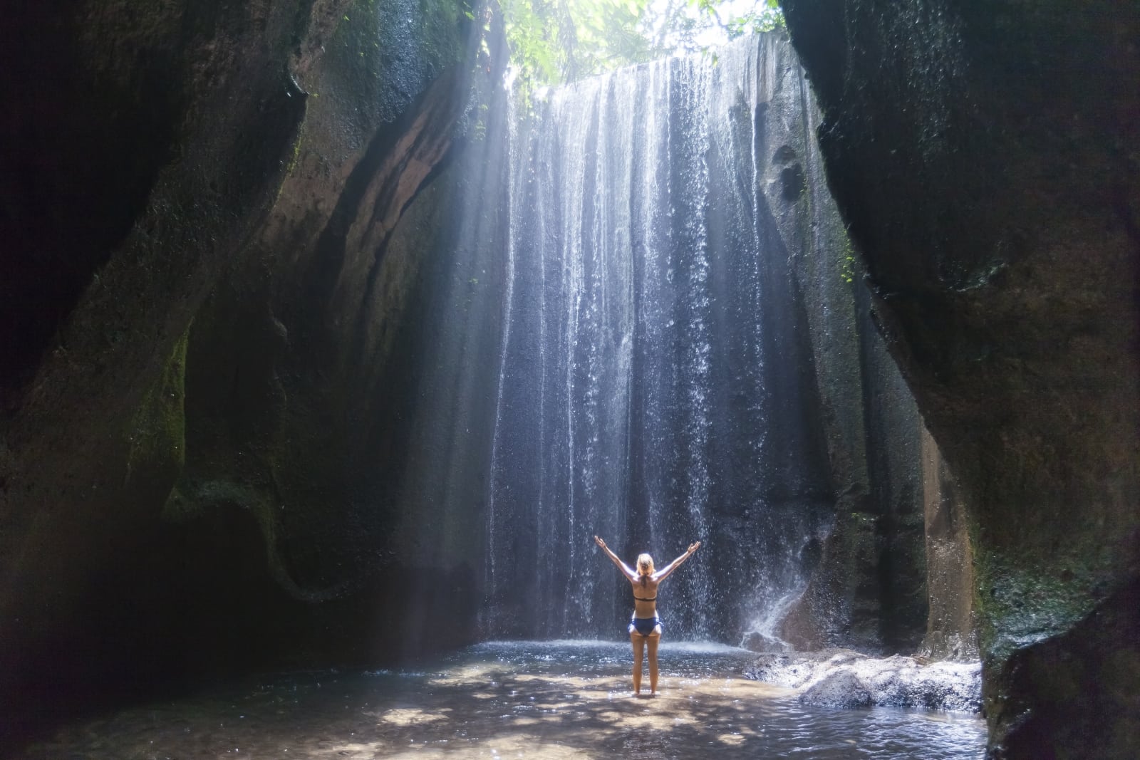 image of woman traveller with arms up in the air near waterfall