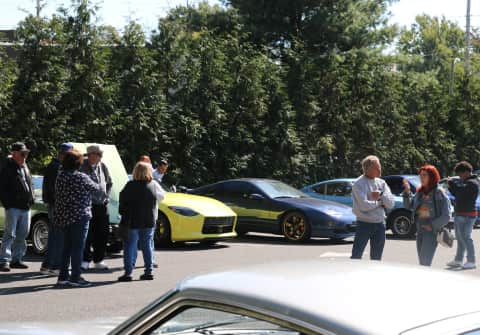 Z Car enthusiasts talking in groups, with their Z cars in the foreground and a 2023 Z Proto Spec in the background.