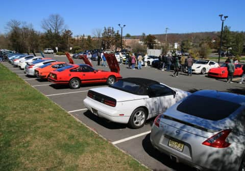 30 Z cars lined up in two rows with 3 New Z's (black, white and yellow), with a silver 350Z in the foreground, flanked by a white 300ZX convertible, and a red 280ZX turbo t-top.