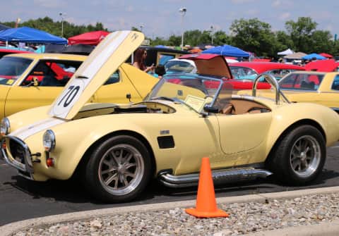 A pale yellow Cobra with a white hood stripe, Halibrand mag wheels, chrome side pipes & roll bar