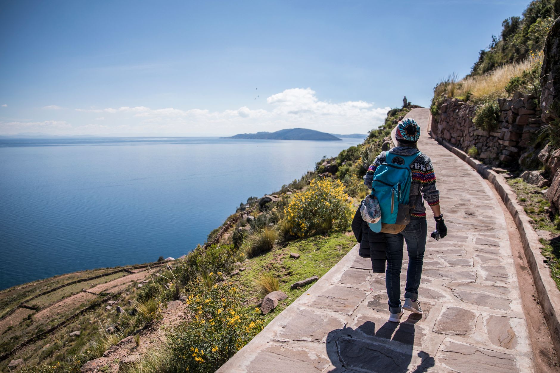 Randonneuse sur un chemin dallé à flanc de colline de l’île de Taquile, le lac Titicaca en contrebas