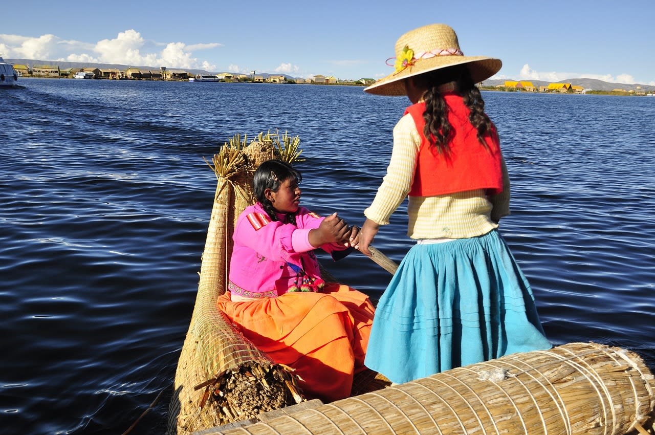 Deux femmes uros en tenue traditionnelle sur une barque en roseaux de totora, îles flottantes du lac Titicaca en arrière-plan