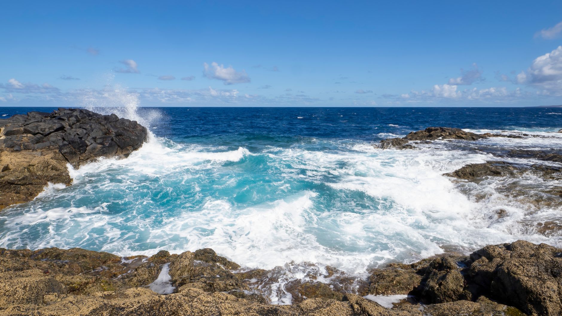 Vagues écumantes qui se brisent entre des roches noires et déchiquetées sous un ciel dégagé