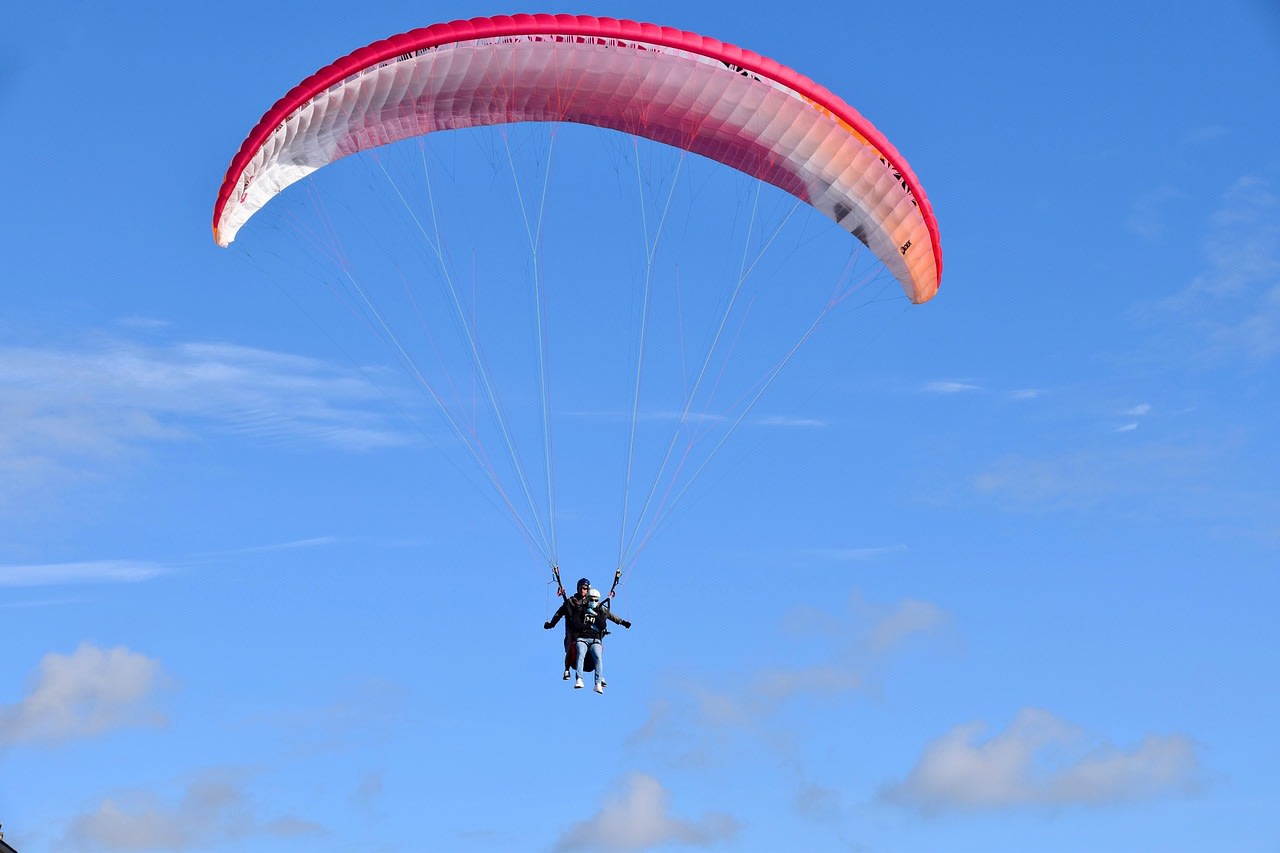 Parapente biplace en vol dans un ciel bleu, le passager assis devant le moniteur sous la voile