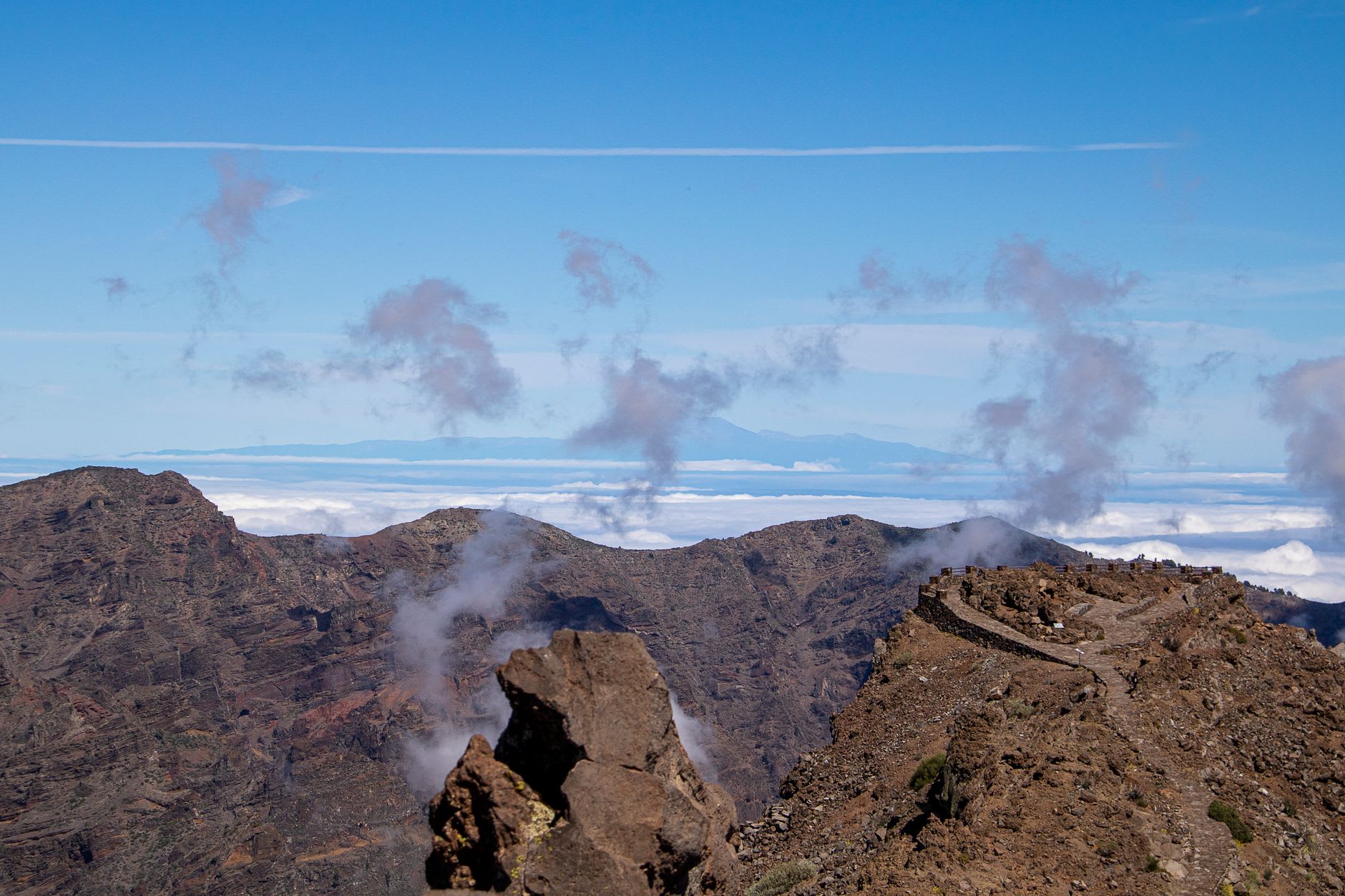 Crête volcanique et large mer de nuages vues d’un belvédère d’altitude, silhouette d’un haut volcan à l’horizon sous un ciel bleu