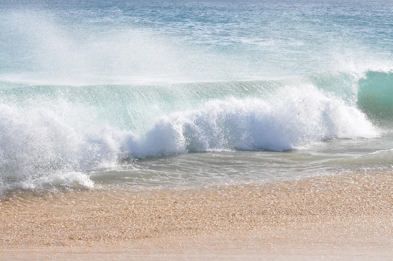Rouleau qui déferle et explose en écume blanche à quelques mètres du sable, gros plan sur la vague