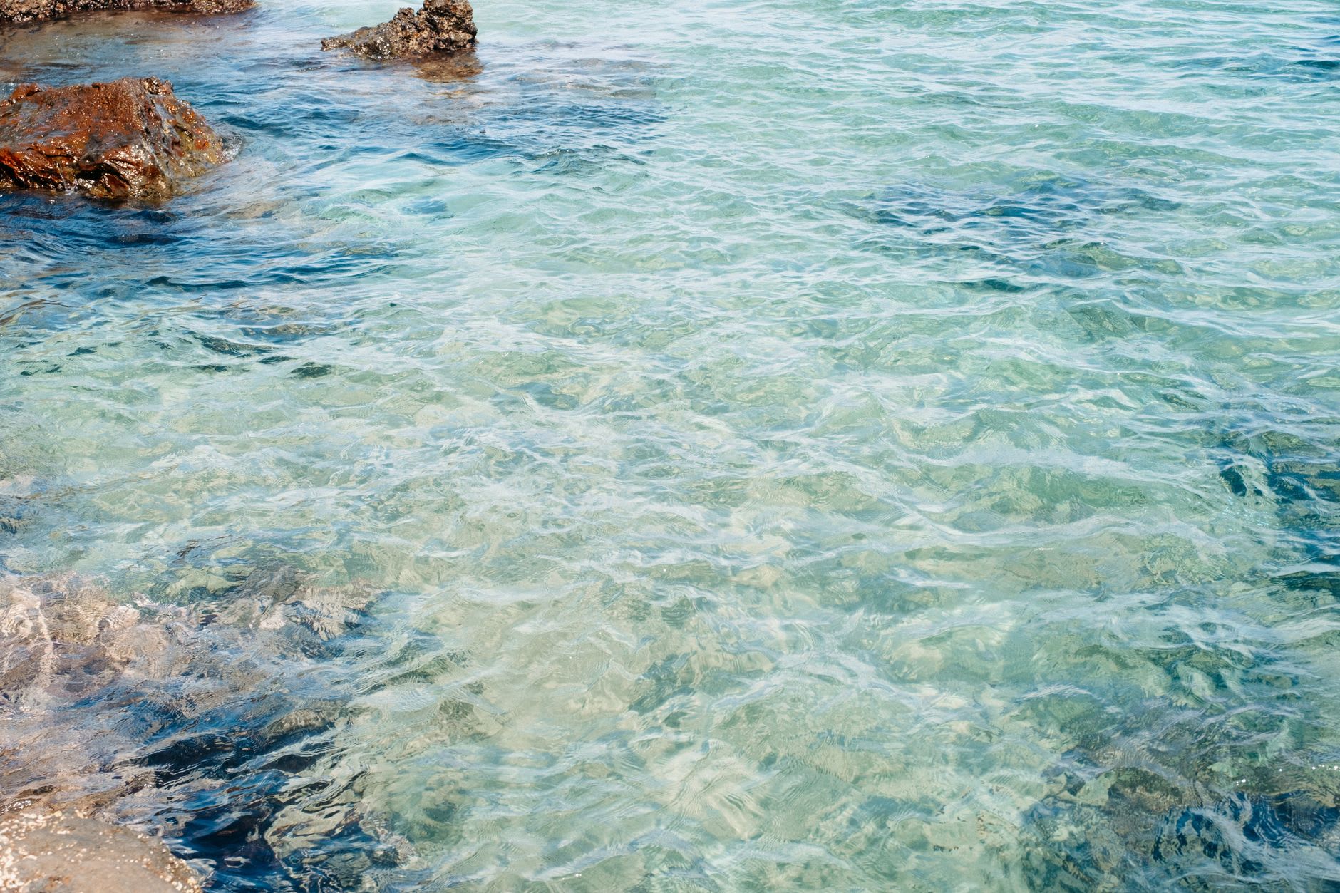 Eau peu profonde et limpide aux reflets turquoise passant sur des rochers plats affleurant près du bord