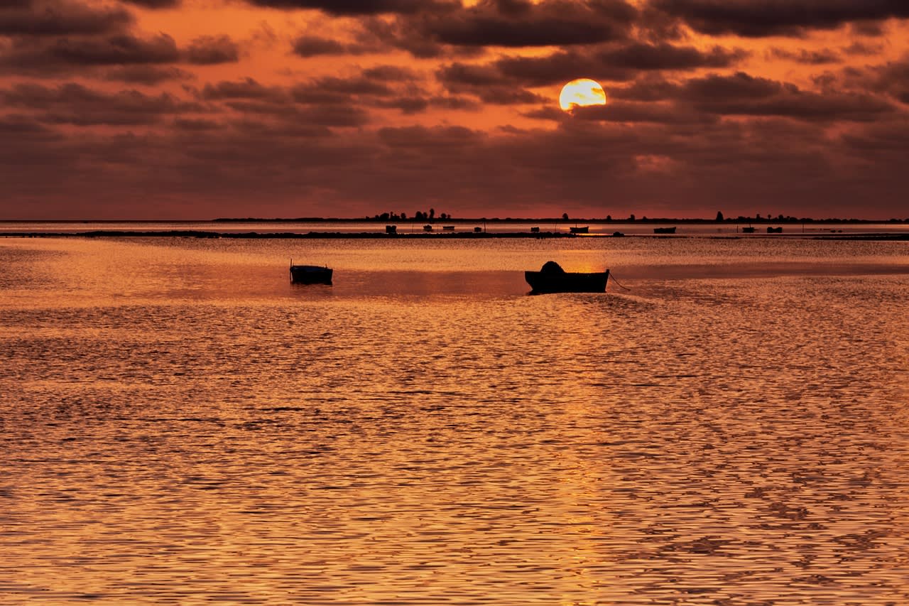 Barques immobiles sur une eau peu profonde sous un ciel orange strié de nuages au couchant