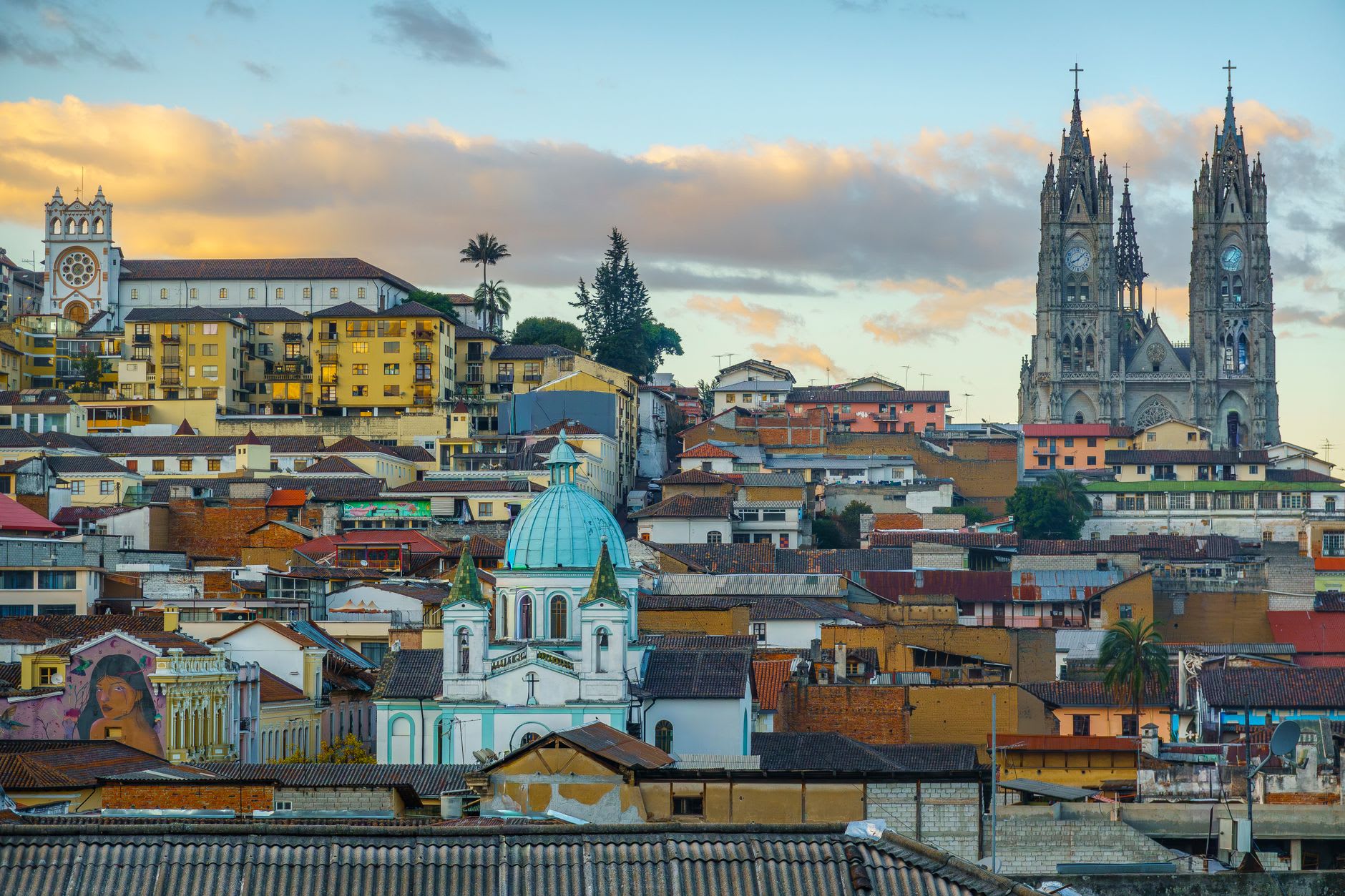 Toits de tuiles de la vieille ville de Quito au crépuscule, dominés par les tours néogothiques de la basilique du Vœu national