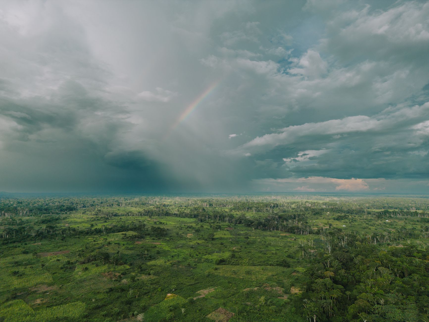 Grain de pluie sombre crevant au-dessus d’une plaine forestière équatoriale, arc-en-ciel partiel dans le rideau d’averse