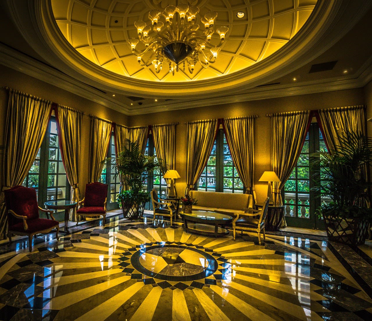 Salon d’hôtel coiffé d’une coupole dorée, lustre monumental et sol de marbre en étoile noir et blanc