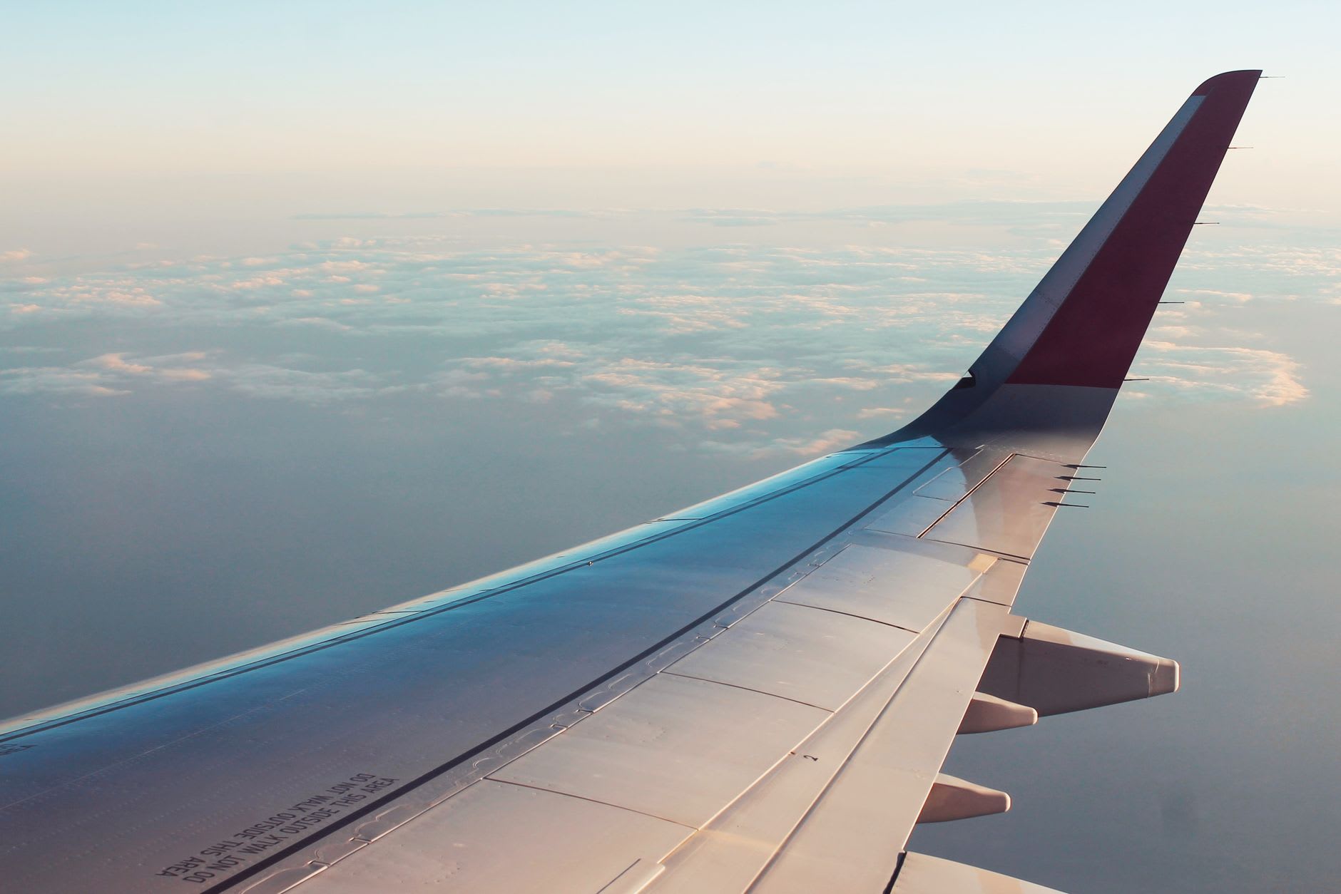 Aile d’avion de ligne et son winglet bordeaux au-dessus d’une couche de nuages en fin de journée
