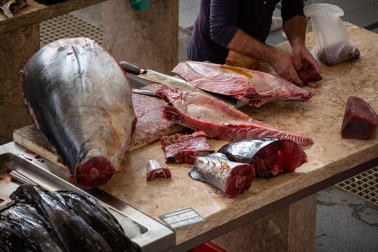 Étal de poissonnier du marché de Funchal, gros thon découpé au couteau sur un plan de marbre, tranches de poisson rouge posées à côté