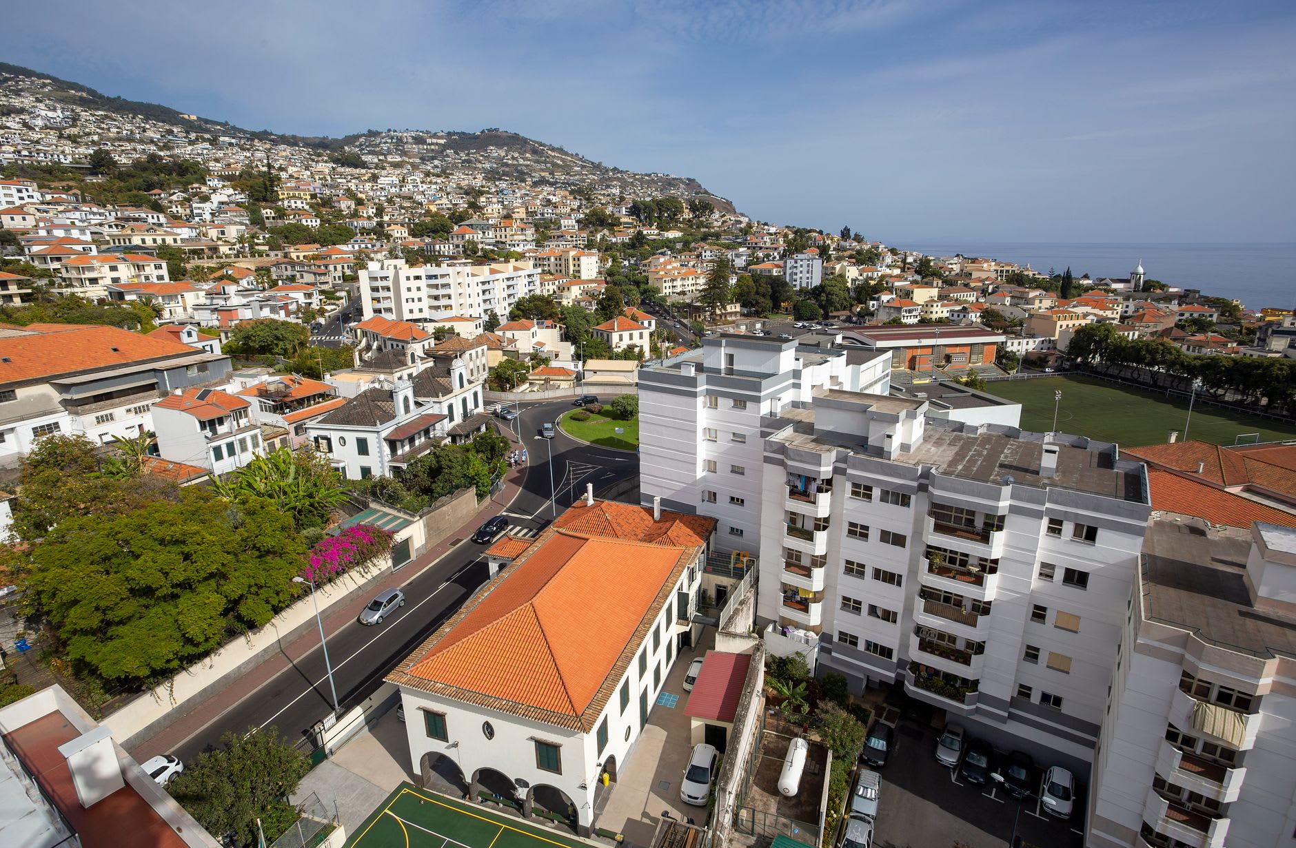 Vue aérienne de Funchal, ses toits de tuiles rouges étagés sur la colline verte descendant vers l’océan sous un ciel bleu