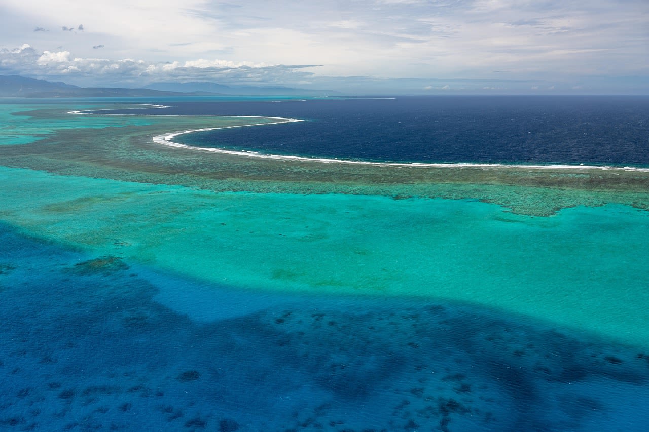 Vue aérienne d’un lagon turquoise protégé par une barrière de corail, la houle brisant sur le récif avant l’océan profond