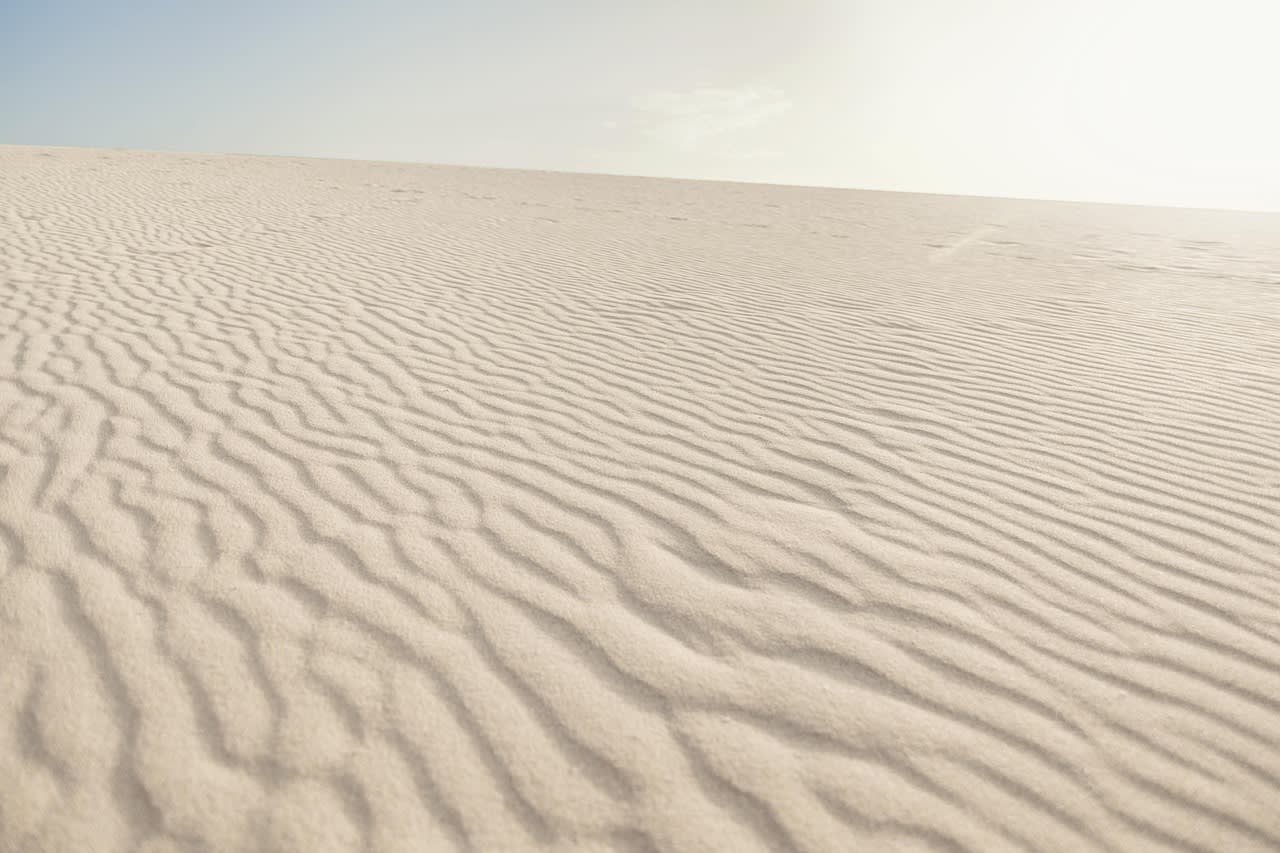 Rides régulières dessinées par le vent à la surface d’une vaste étendue de sable clair