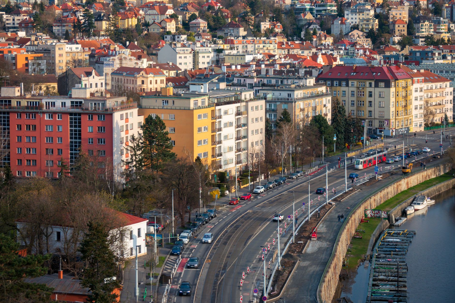 Quai de la Vltava vu d’en haut, un tram rouge longe la berge devant les immeubles pragois aux arbres nus en hiver