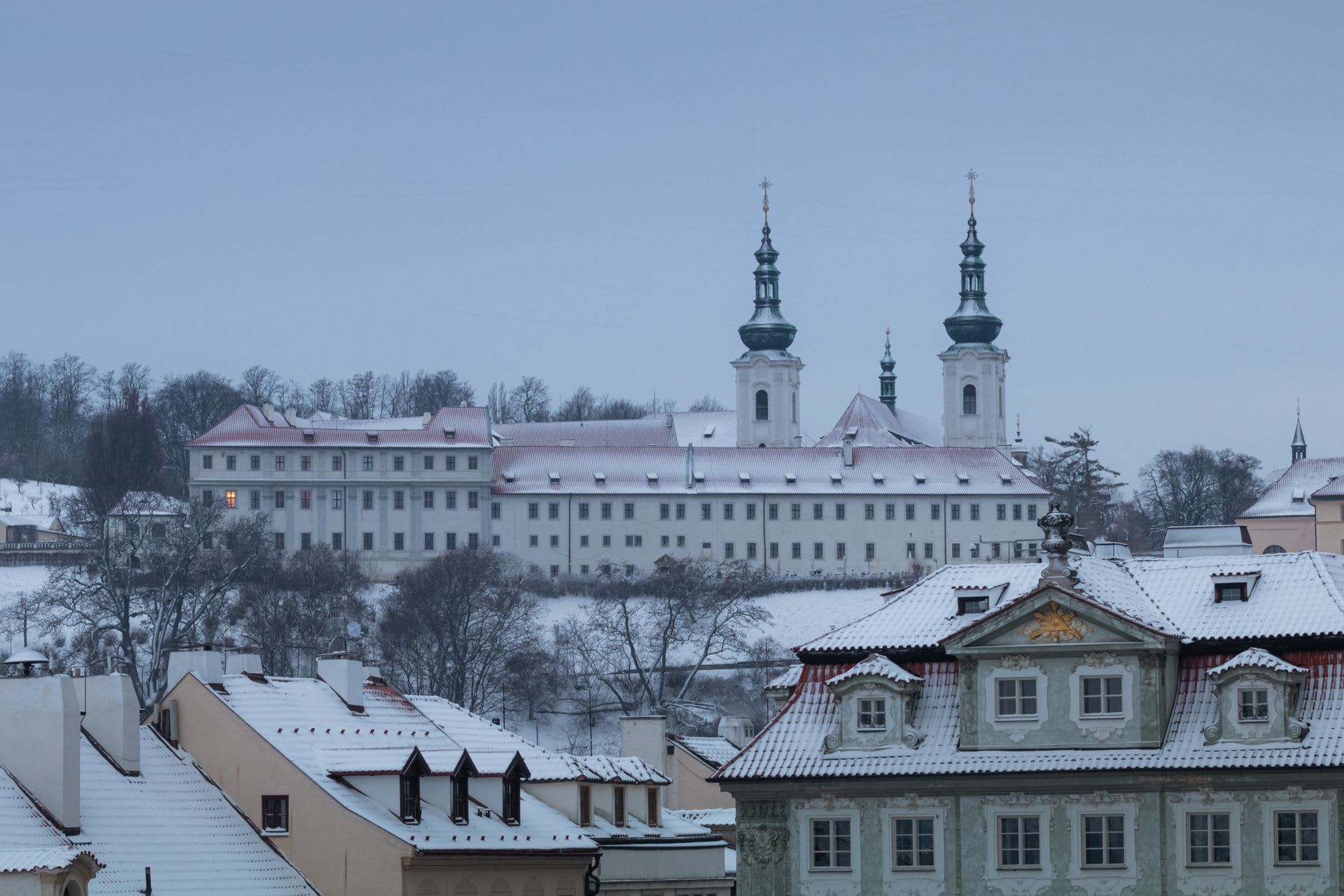 Les deux tours baroques du monastère de Strahov au-dessus de toits rouges saupoudrés de neige à la tombée du jour