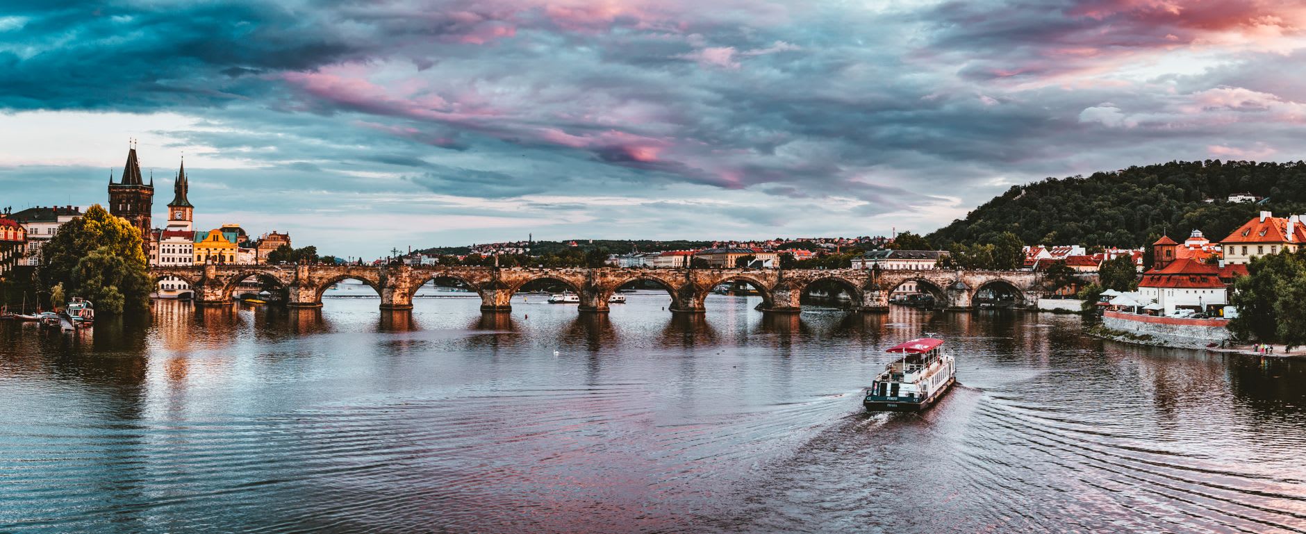 Pont Charles et ses arches sous un ciel d’orage rose et gris en fin de journée, bateau de croisière sur la Vltava