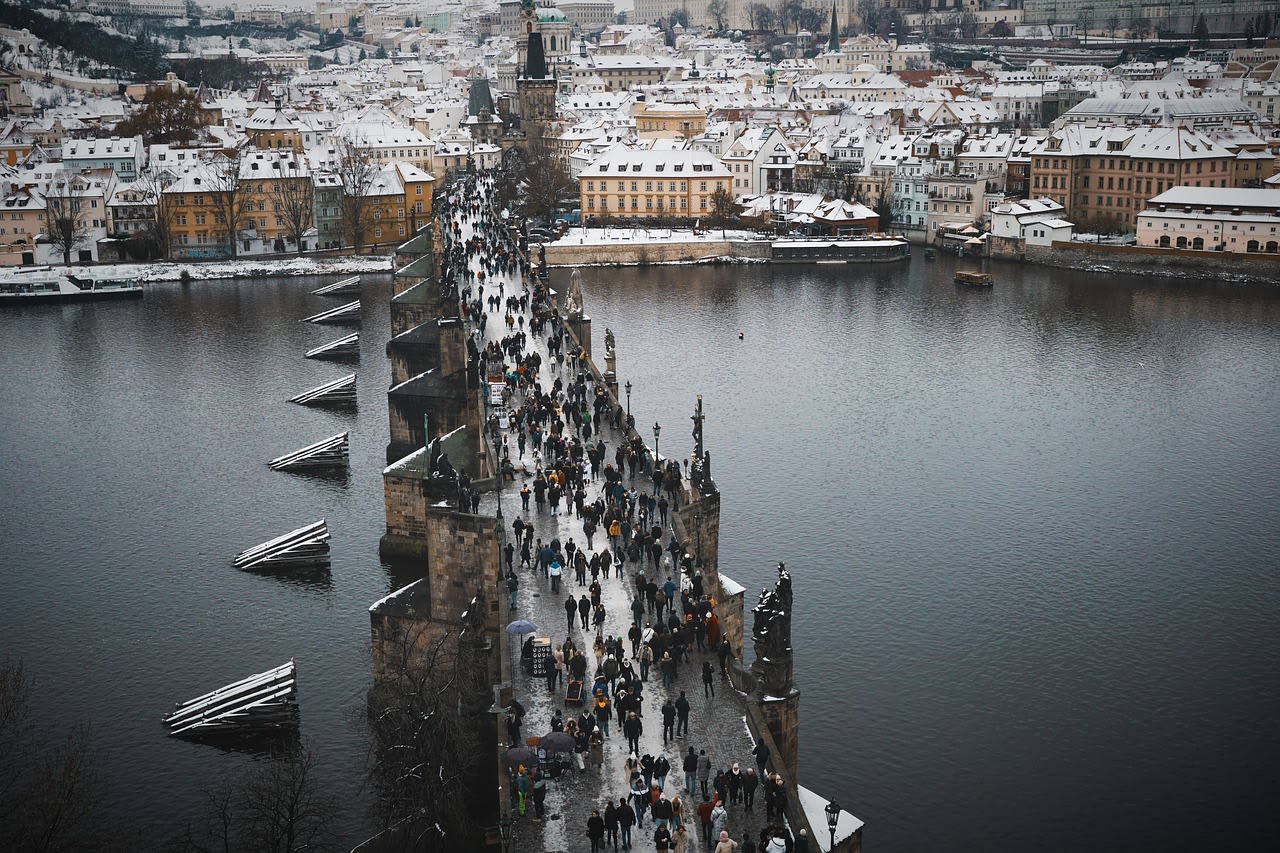 Toits enneigés de Malá Strana et pont Charles noir de monde vus d’en haut sous un ciel d’hiver