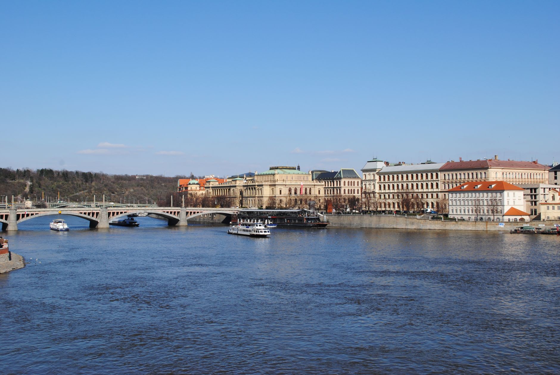 Bateaux de promenade sur la Vltava près du pont Mánes, coteau de Letná aux arbres nus sous un ciel bleu