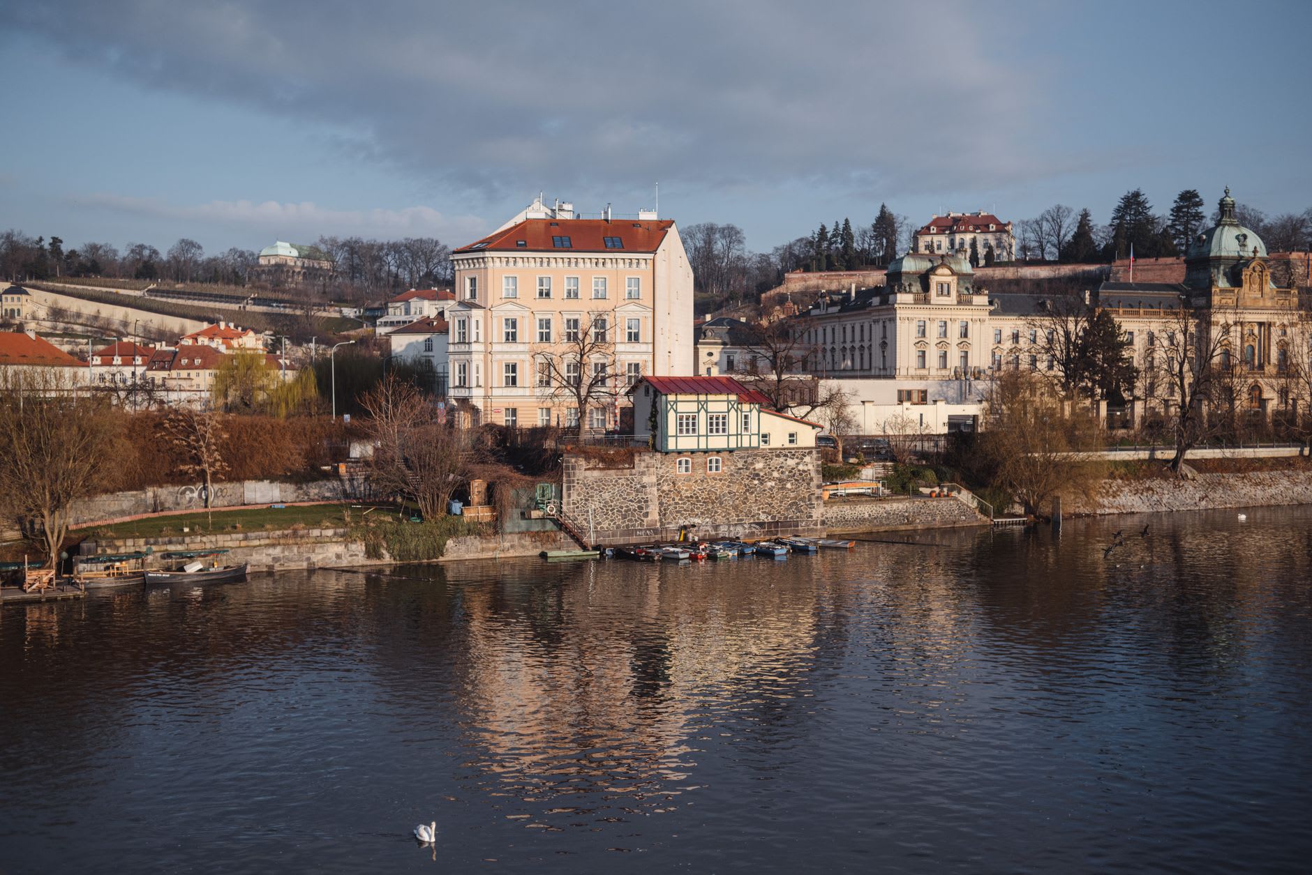Berge de la Vltava sous la colline du château, arbres dénudés et barques amarrées dans la lumière dorée du matin