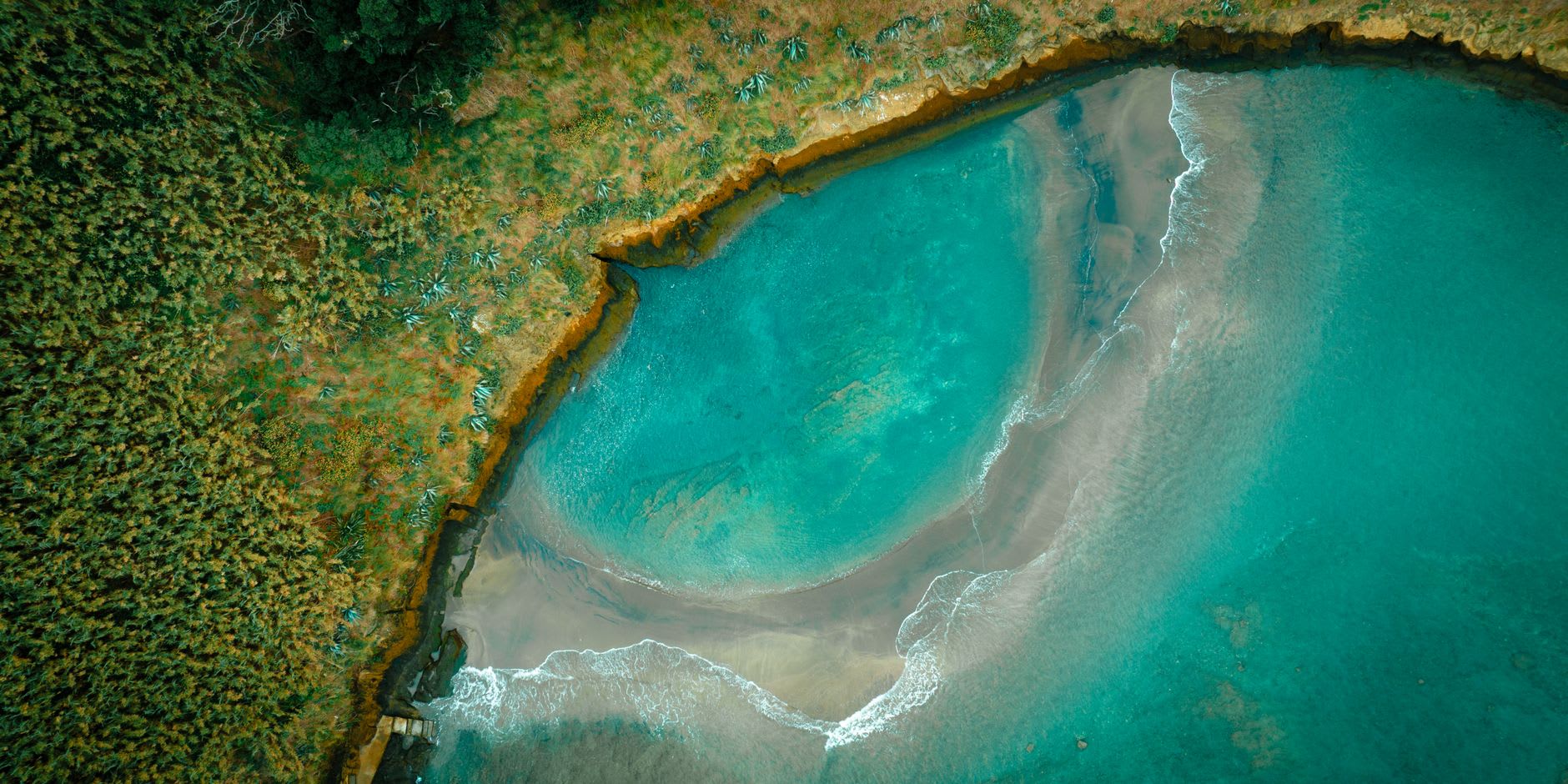 Eau turquoise transparente d’une anse peu profonde bordée de végétation, fond de sable clair et aucune personne à l’eau