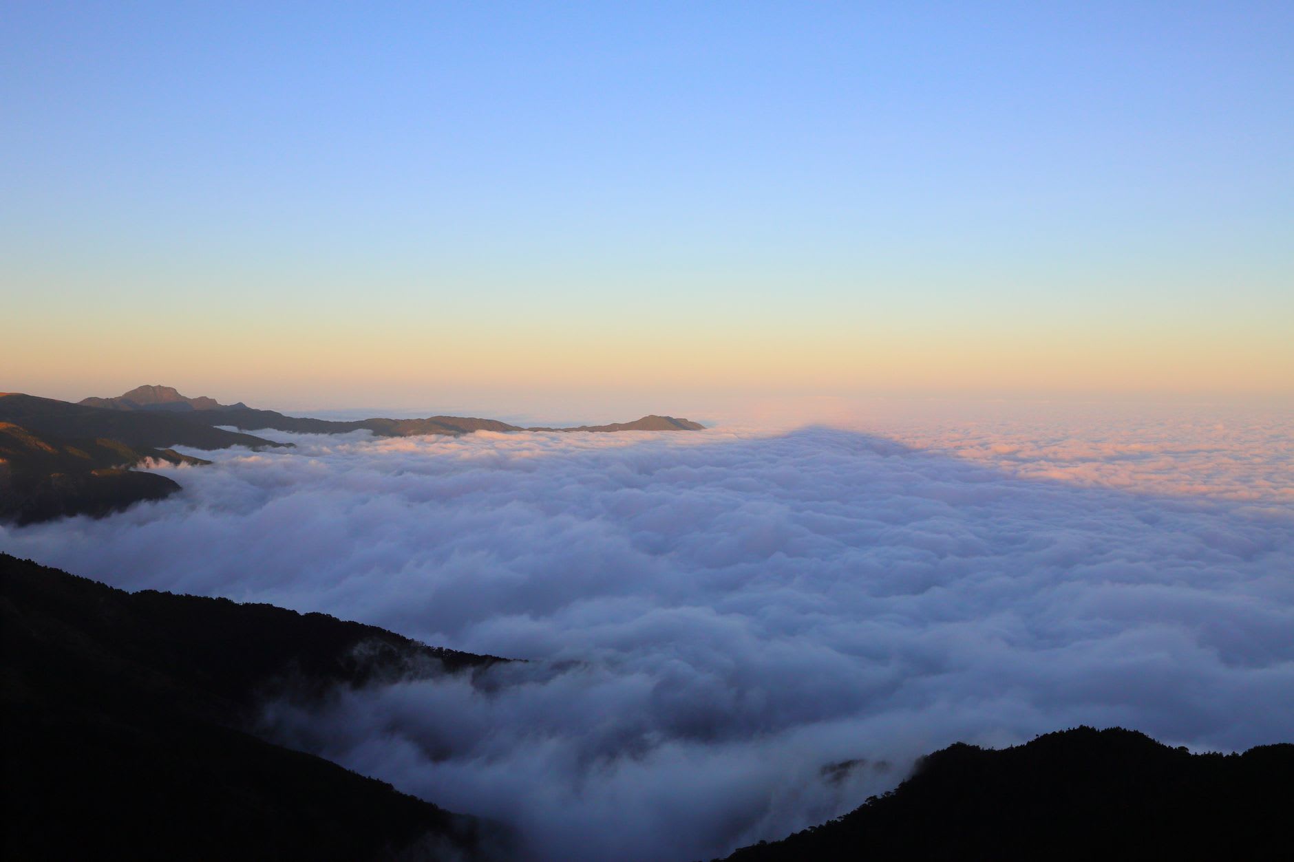 Mer de nuages moutonnante embrasée par le soleil levant, crêtes boisées sombres au premier plan