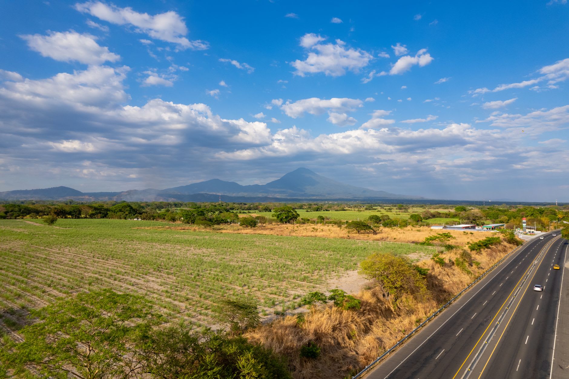 Autoroute à deux voies traversant des champs de canne à sucre, un volcan conique à l’horizon