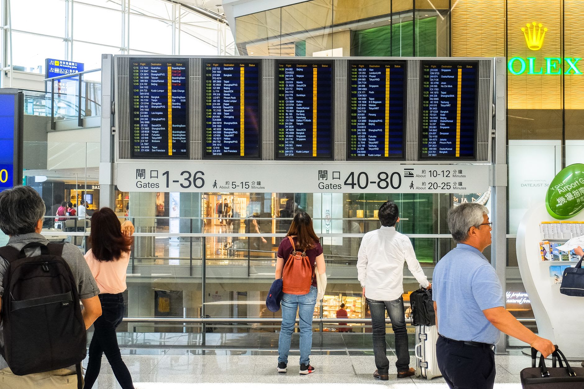 Voyageurs isolés debout devant un grand tableau des départs dans un hall d'aéroport