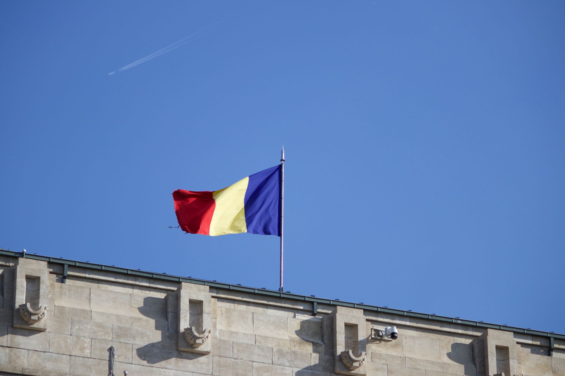 Drapeau roumain à trois bandes verticales bleu, jaune et rouge flottant sur un mât en haut d’un bâtiment en pierre sous un ciel dégagé