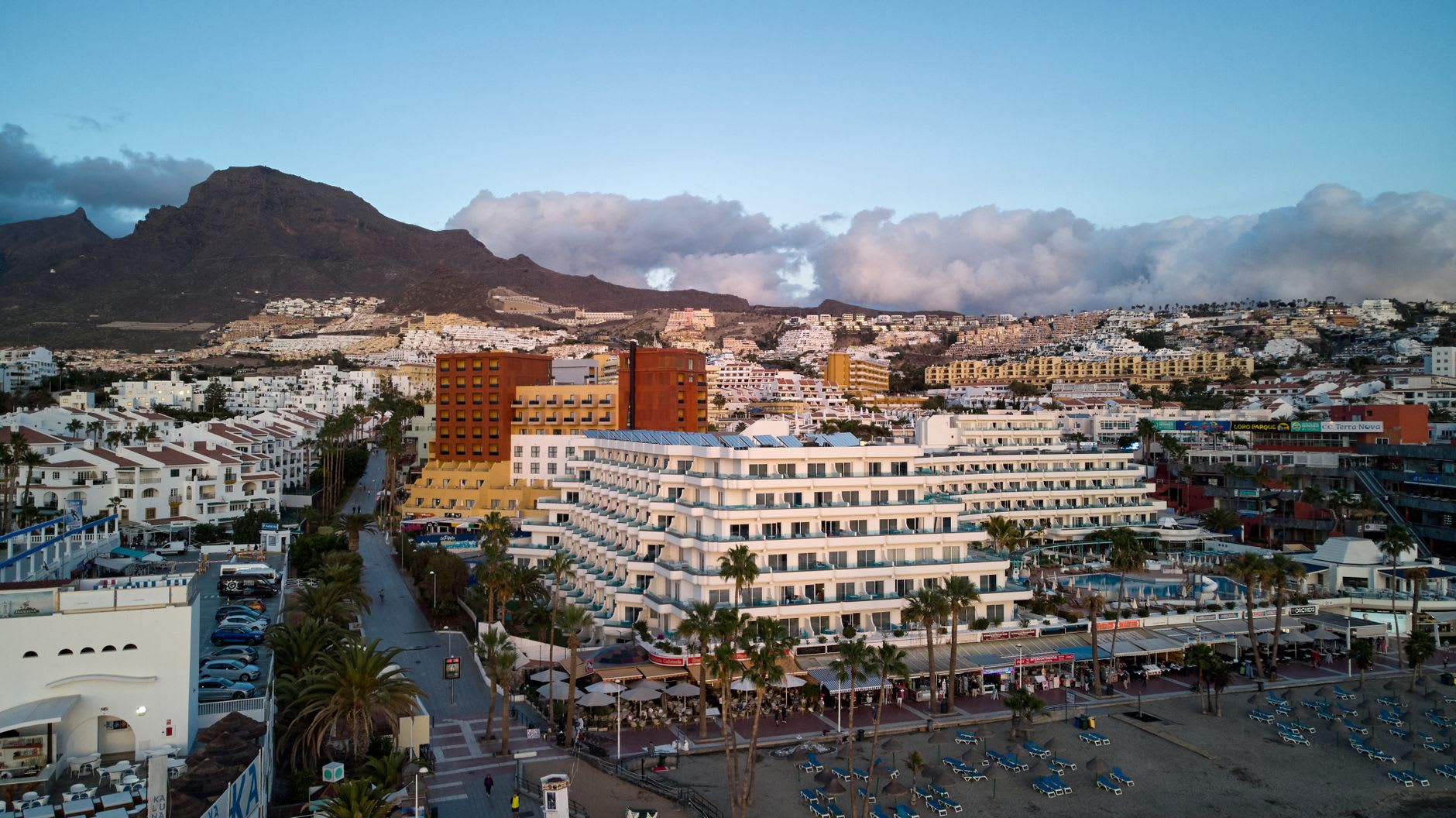 Vue aérienne au crépuscule d’une station balnéaire au bord de l’eau, un long banc de nuages posé sur la crête des montagnes