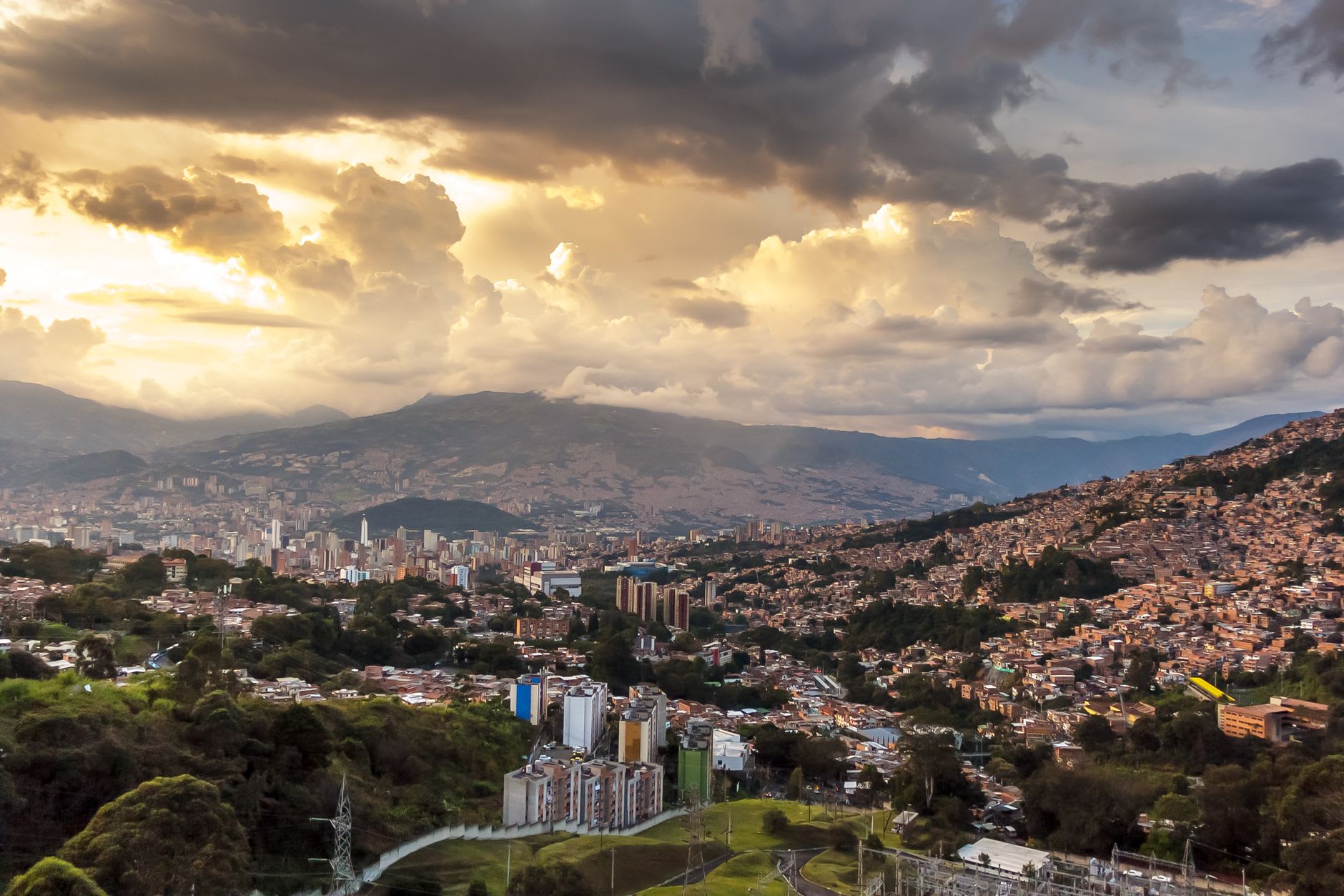 Medellín au fond de sa vallée andine au coucher du soleil, quartiers grimpant sur les collines sous des nuages d’orage