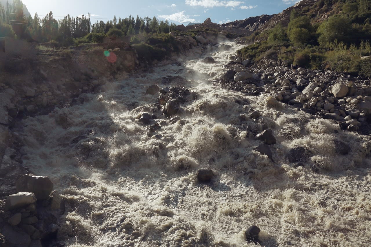 Torrent de montagne chargé de limon dévalant un lit de gros blocs entre deux berges caillouteuses