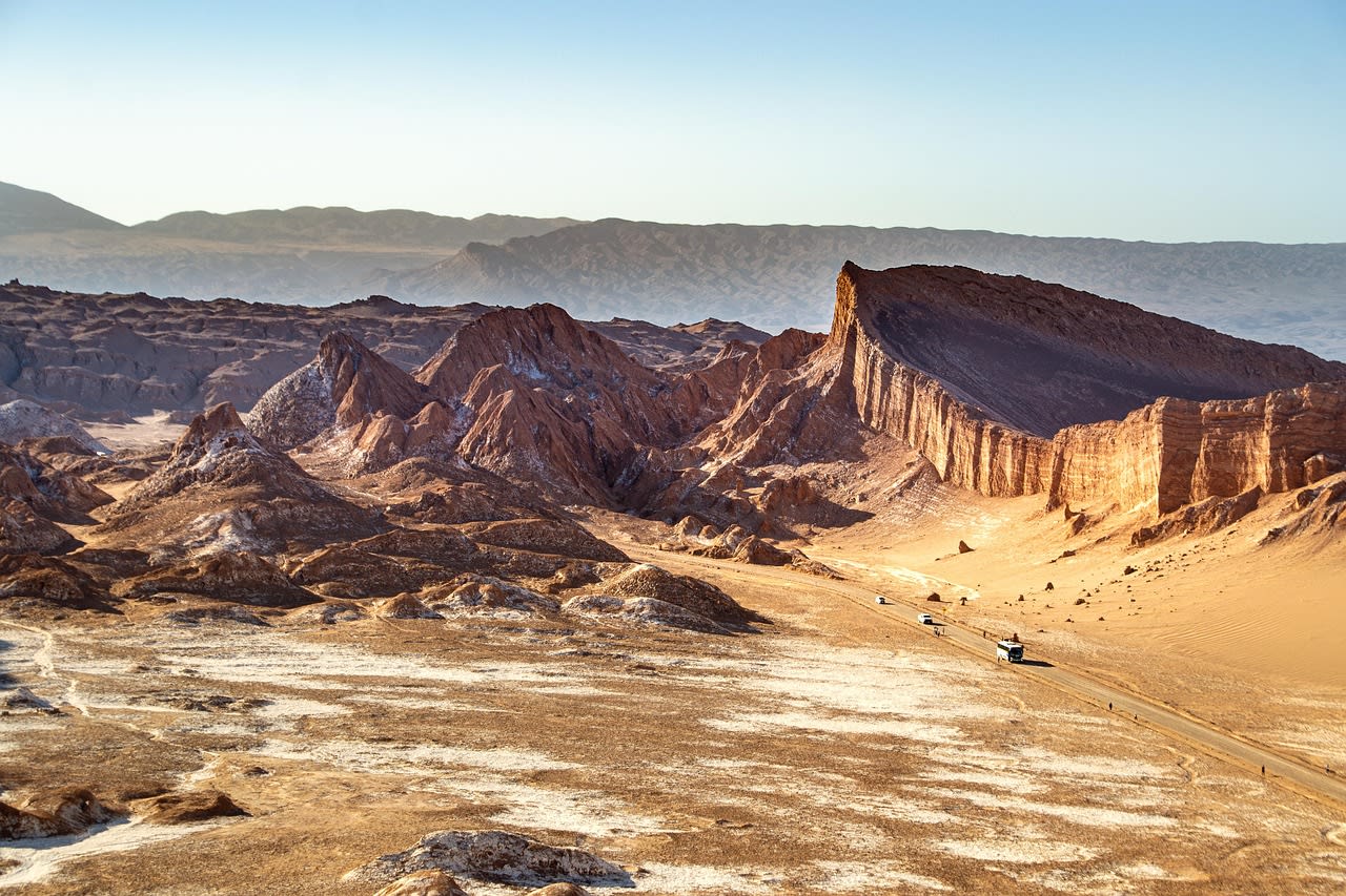 Crêtes de sel et falaises ocre de la Valle de la Luna, avec la piste et deux minibus de tour au loin