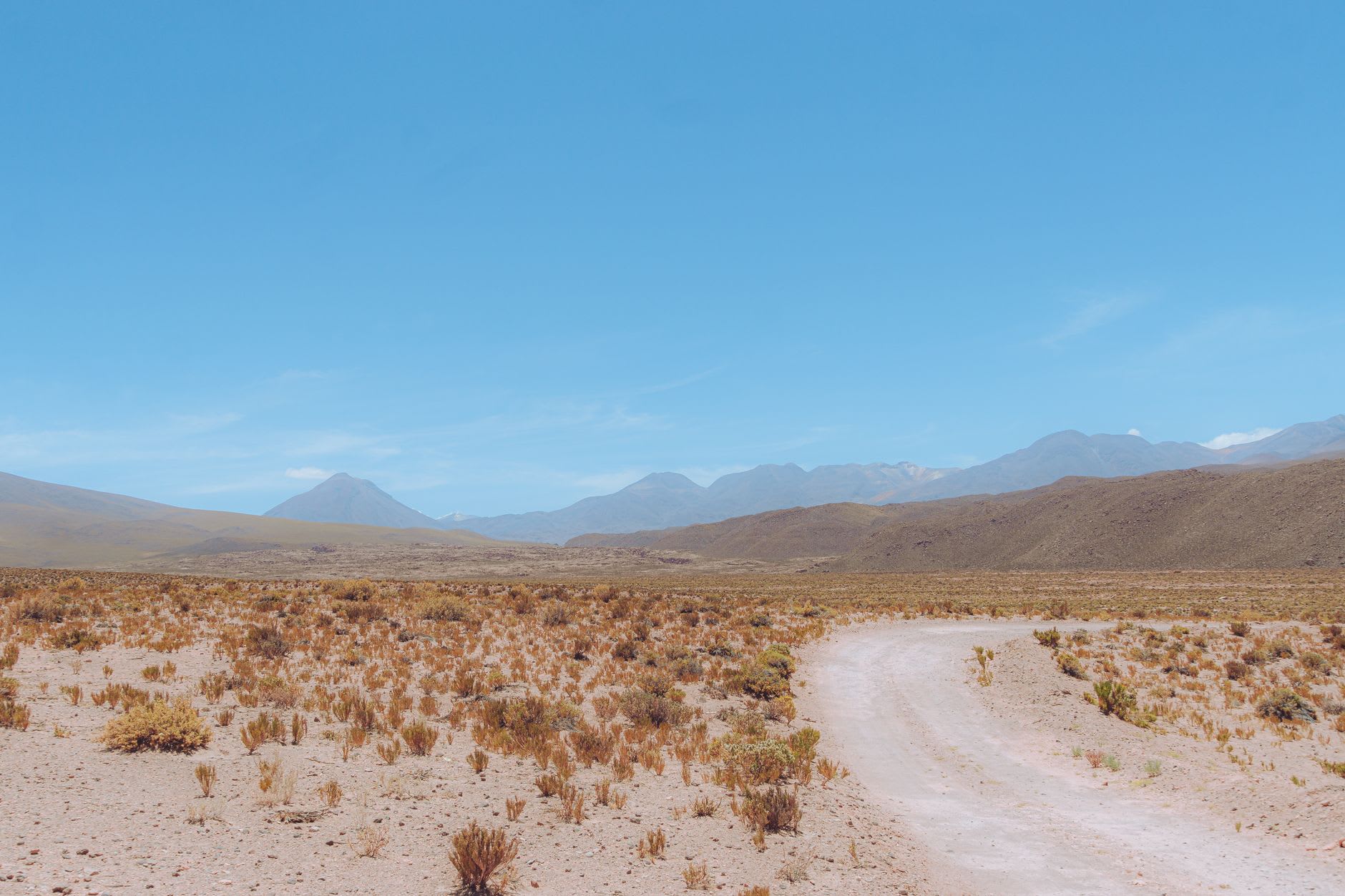 Piste de terre sans revêtement traversant l'altiplano désertique, sommets andins à l'horizon