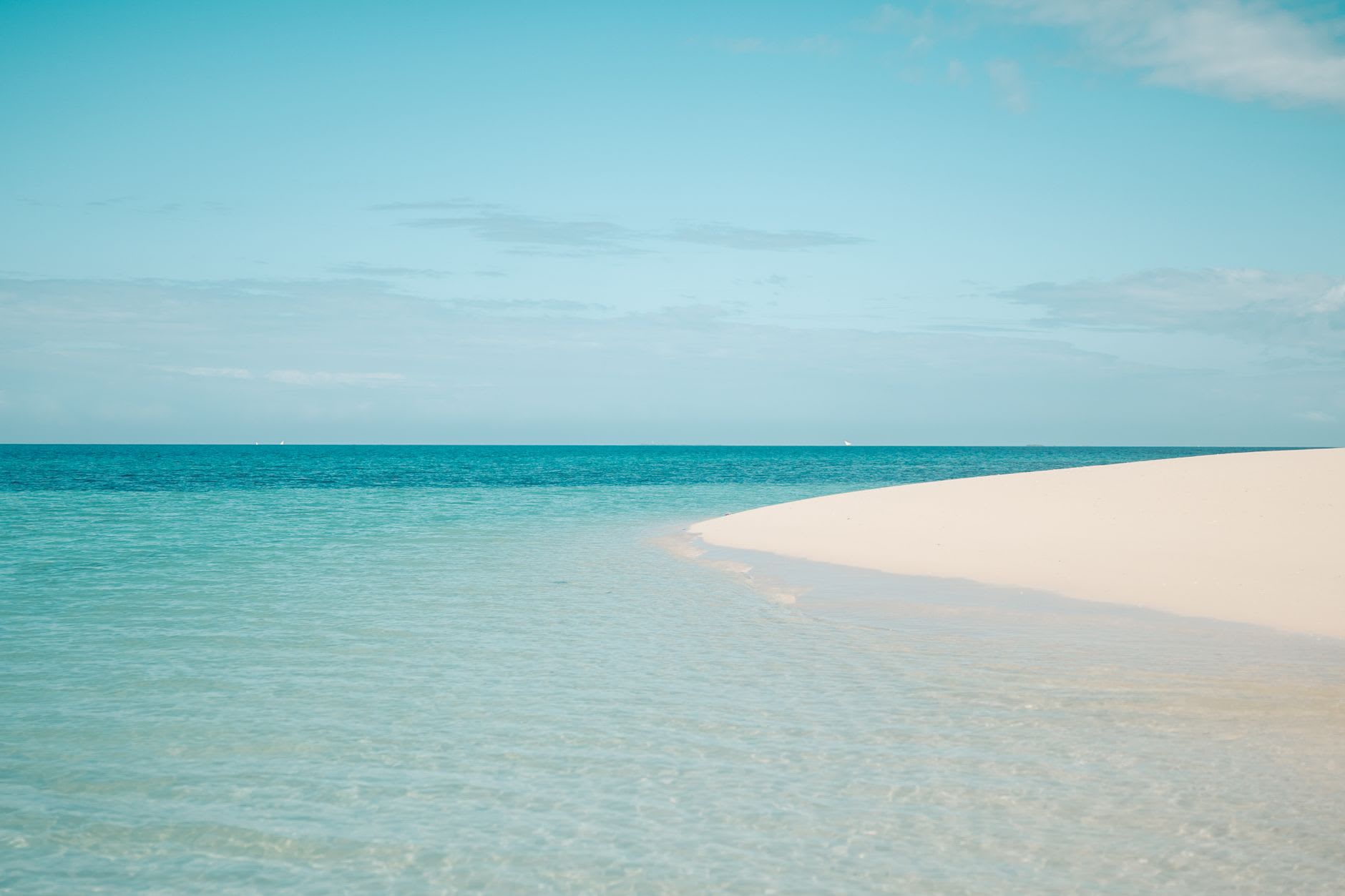 Banc de sable blanc bordé d’un lagon turquoise peu profond sous un ciel clair